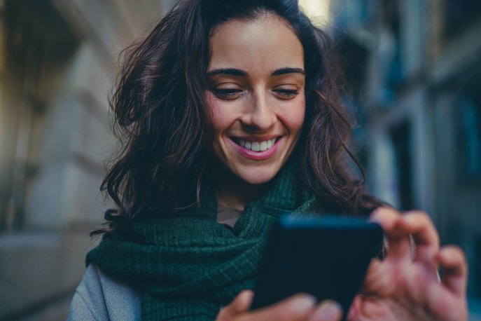 Dame som smiler mot telefonen, viser hvor enkelt det er å bruke appen APCOA FLOW for å utvide parkeringen