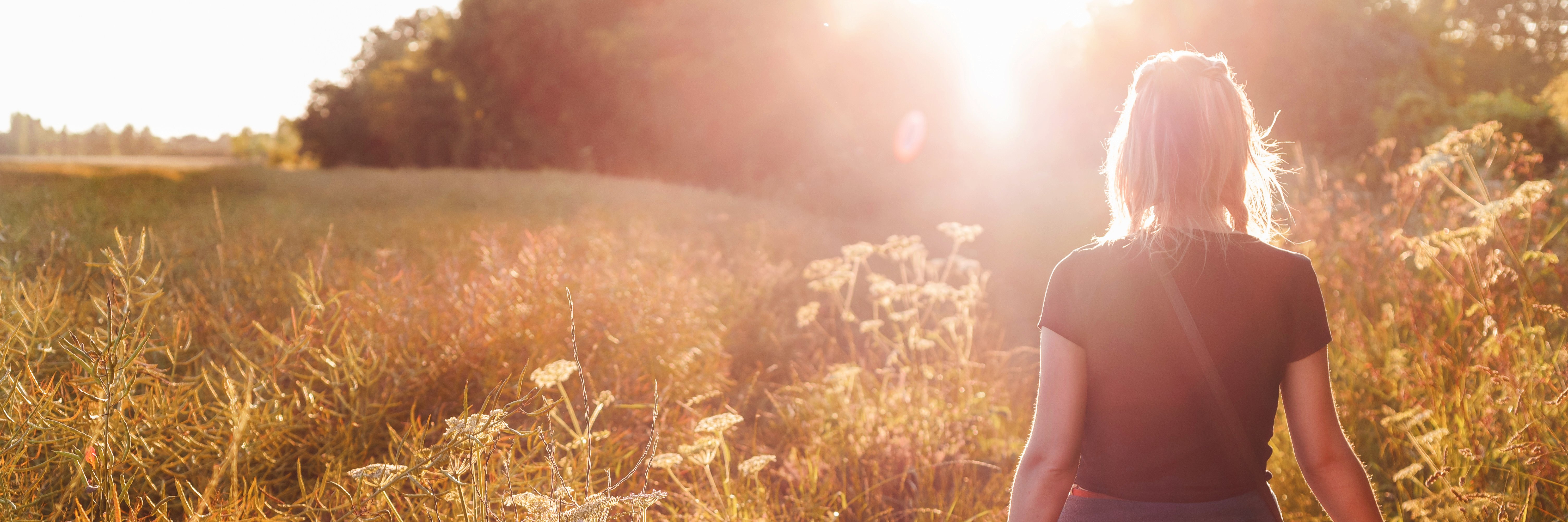 Kvinne går i naturlig landskap i sollys. Et symbol på bærekraft og miljøbevissthet hos APCOA